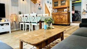 A cozy living room with a wooden dining table, white chairs, a sofa, and a wooden cabinet with glass doors. - The House of the Beach (Les Sables-d´Olonne)