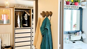 A room with a surf-themed decor, including a surfboard and a 'SURF' sign. There is a wardrobe with a 'FAMILLE' sign, a mirror with a view of the outside, and a bathroom with a sink and toiletries. - The House of the Beach (Les Sables-d´Olonne)