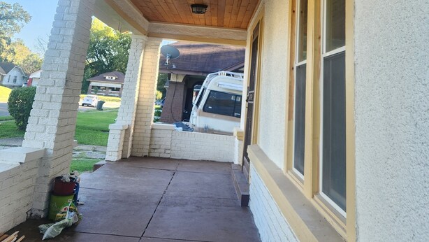 A covered porch with a ceiling fan, a concrete floor, and a white brick wall.