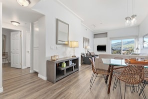 A modern living room with a dining area, a large mirror, and a view of the outdoors.