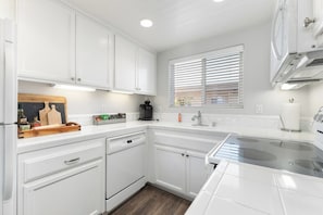 A modern kitchen with white cabinetry, a built-in dishwasher, and a stainless steel range hood.