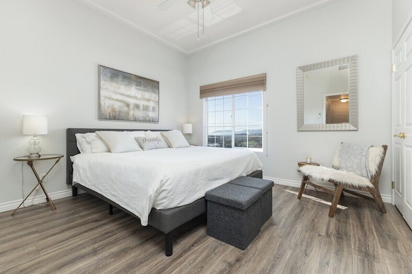 A bedroom with a bed, bedside tables, a chair, a window, and a painting on the wall.