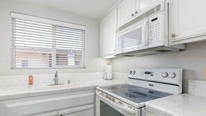 A kitchen with a stove, oven, microwave, and a window with blinds.