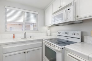 Una cocina con estufa, horno, microondas y una ventana con persianas.