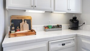 A kitchen with white cabinetry, a wooden cutting board, a coffee maker, and a small chalkboard with writing.