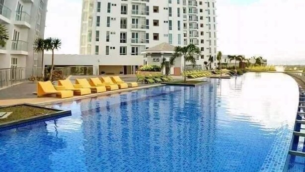 A modern hotel with a swimming pool, multiple floors, and a clear sky.
