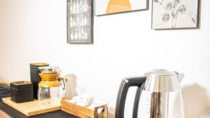 A coffee station with a kettle, a coffee maker, and a tray with coffee cups and a box of coffee pods.