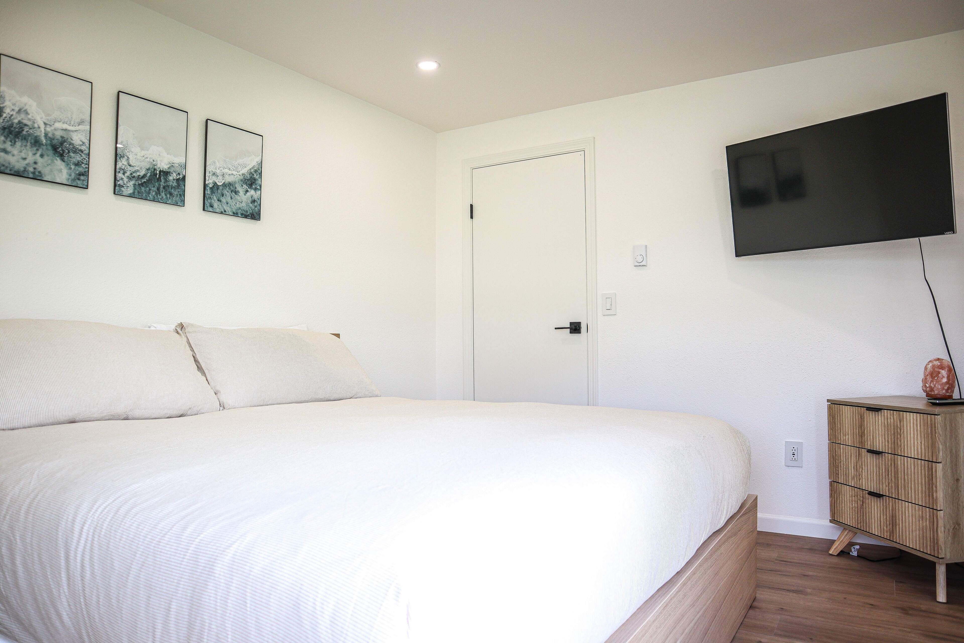A bedroom with a bed, a TV mounted on the wall, and a wooden nightstand.