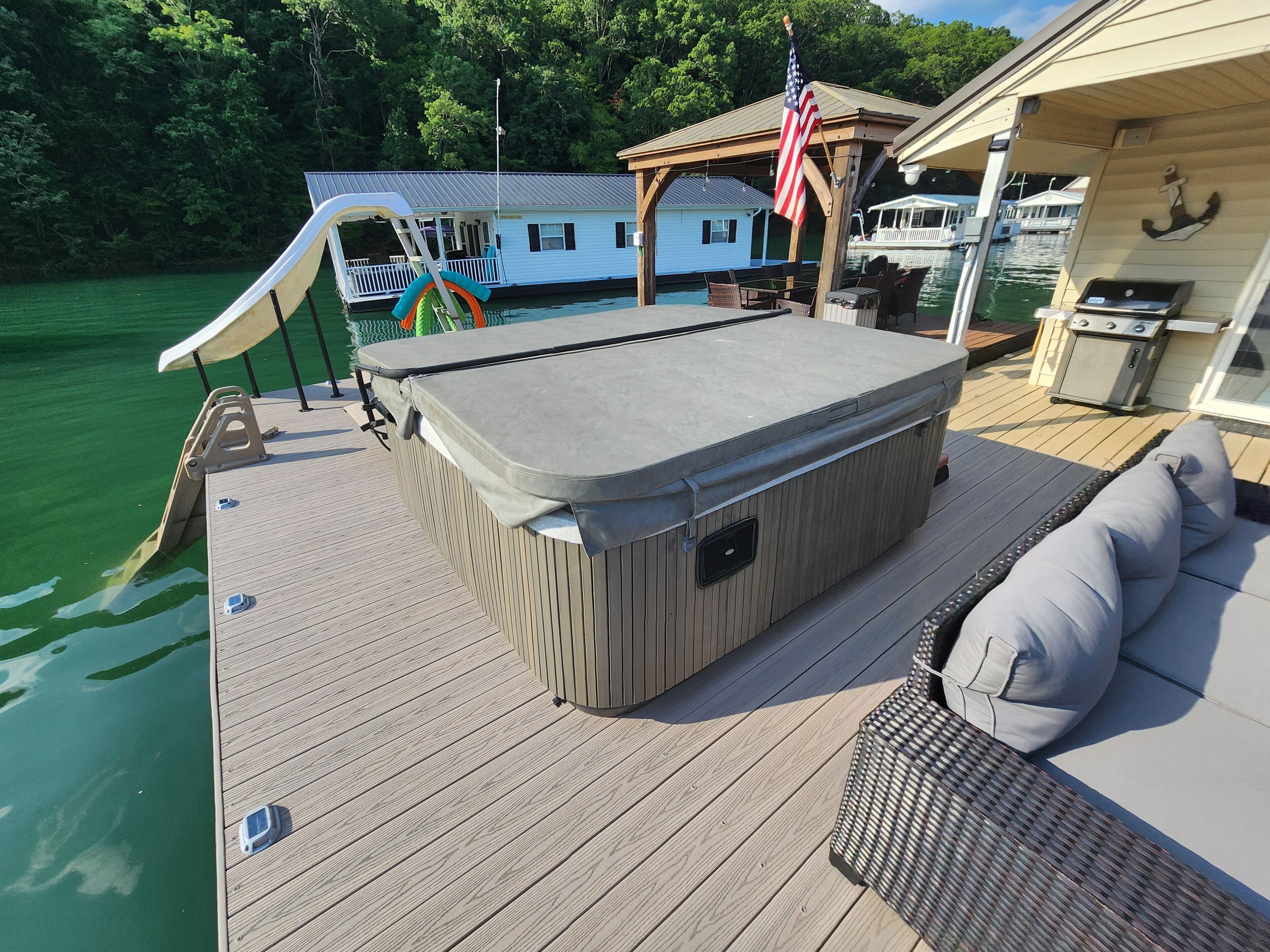 Un bain à remous sur une terrasse en bois, avec vue sur un quai et une maison en arrière-plan.