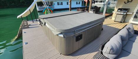 Un bain à remous sur une terrasse en bois, avec vue sur un quai et une maison en arrière-plan.