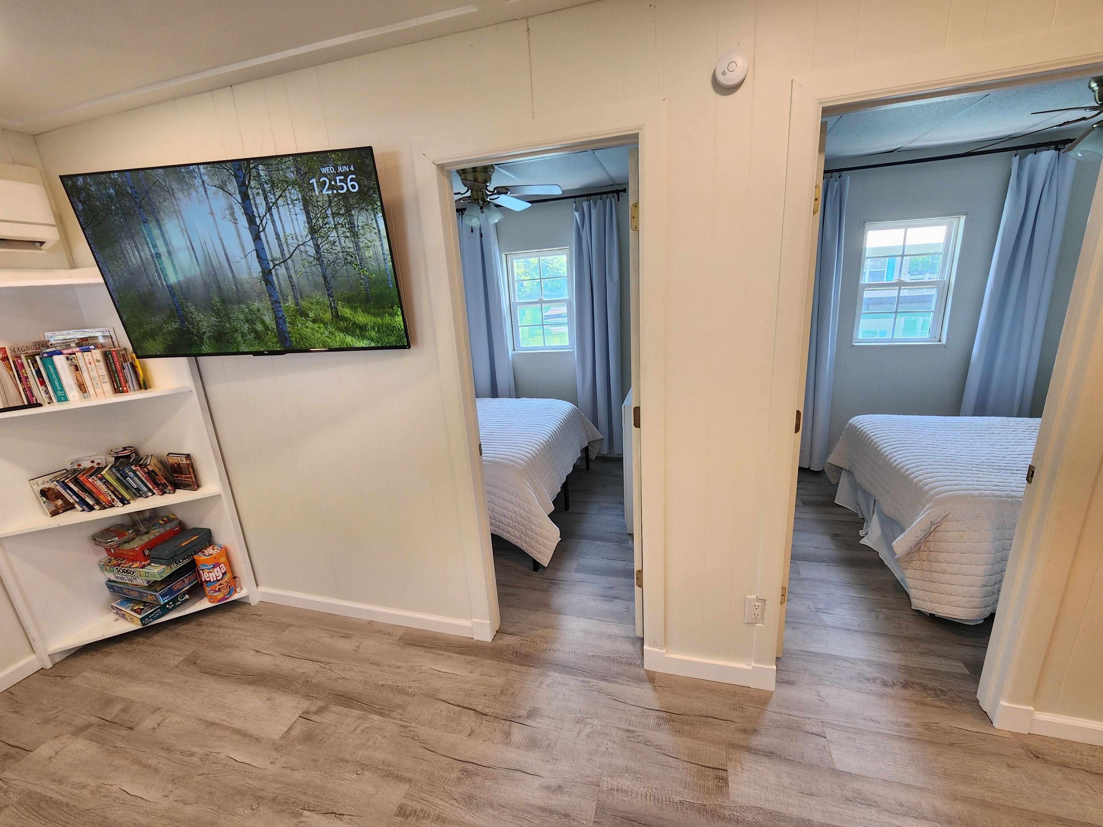 A bedroom with two beds, a bookshelf, and a painting of a forest.
