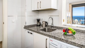 Una cocina moderna con armarios blancos, encimera de granito, cafetera, hervidor y lavavajillas.