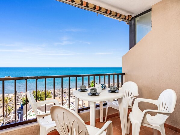 Un balcon avec une table et des chaises, donnant sur une plage et la mer.