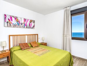 Une chambre d’hôtel avec un lit, une table de chevet, une lampe, un tableau et une fenêtre donnant sur la mer.