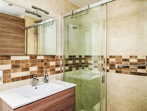 Une salle de bain moderne avec une douche à l’italienne en verre, un lavabo blanc et un meuble-lavabo en bois.