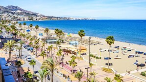 Un paisaje urbano costero con playa, palmeras y un cielo azul despejado.