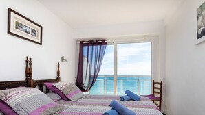 Ein Schlafzimmer mit einem großen Bett, einem Sessel, einem Fenster mit Meerblick und einem gerahmten Bild an der Wand.
