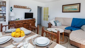 Ein helles Wohnzimmer mit Essbereich, einem Fernseher und einem Gemälde an der Wand.