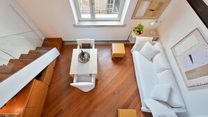 Un salon moderne avec un plancher en bois, un canapé blanc, une petite table et un escalier doté de rampes en verre.