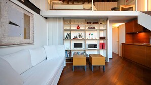 Un espace de vie de style loft avec un canapé blanc, une petite table, une bibliothèque et un coin cuisine.