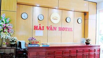 A reception desk with a wooden panel wall, clocks, and a sign for HÀI VÀN HOTEL.