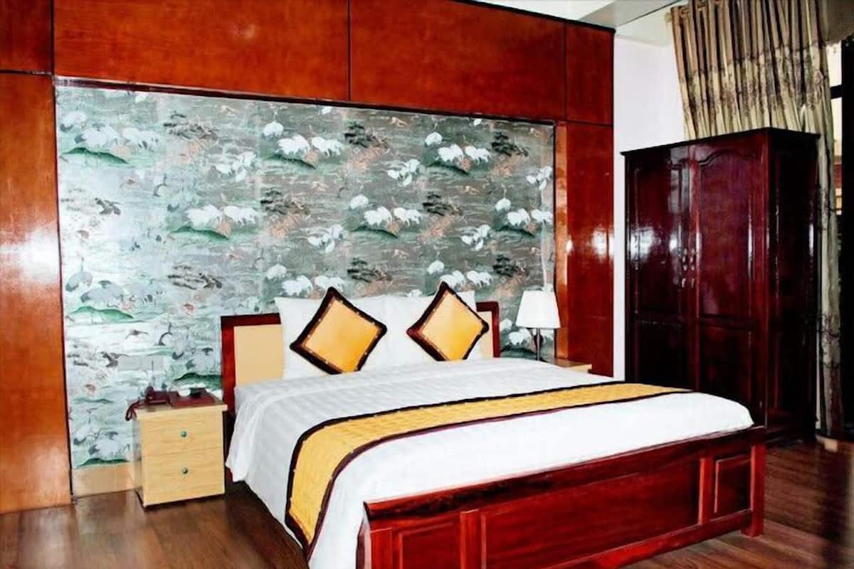 A hotel room with a wooden bed, a nightstand, a lamp, and a wardrobe.