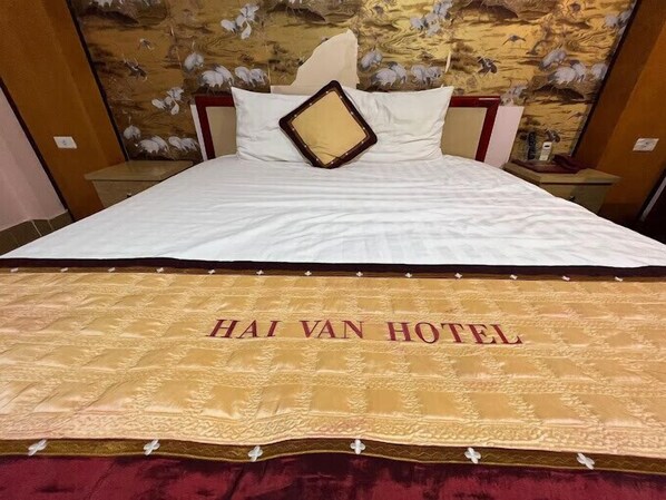 Uma cama de hotel com um edredom branco e o nome "HAI VAN HOTEL" bordado em dourado na parte inferior.