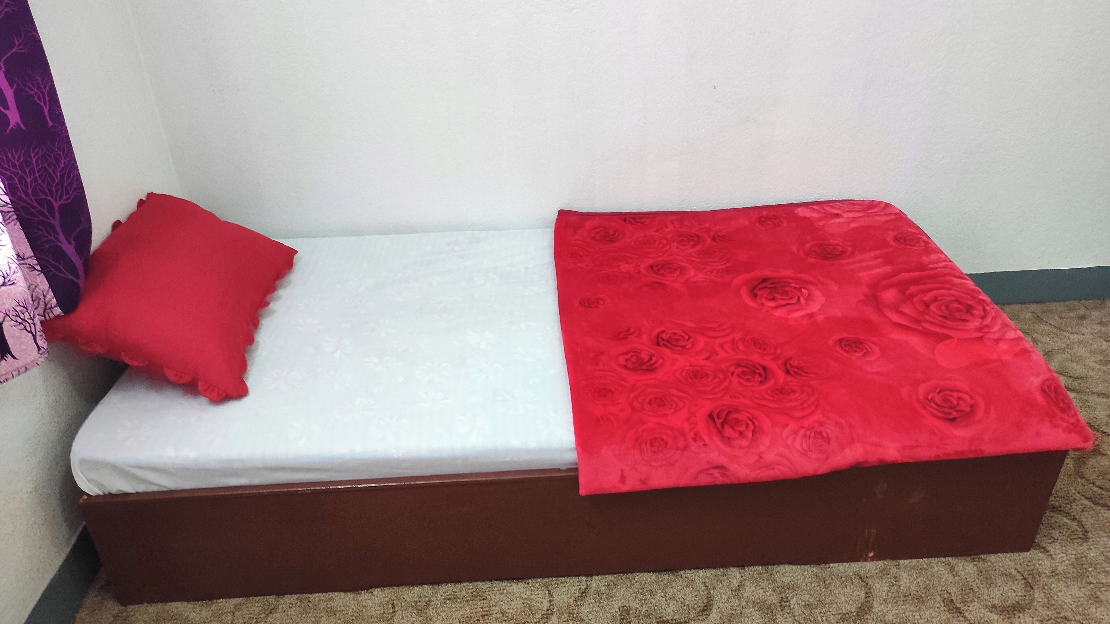 A small bed with a white mattress and a red blanket with a rose pattern.