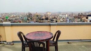 Une terrasse sur le toit, avec une table ronde et deux chaises, d’où l’on peut admirer une vue panoramique sur une ville densément peuplée.