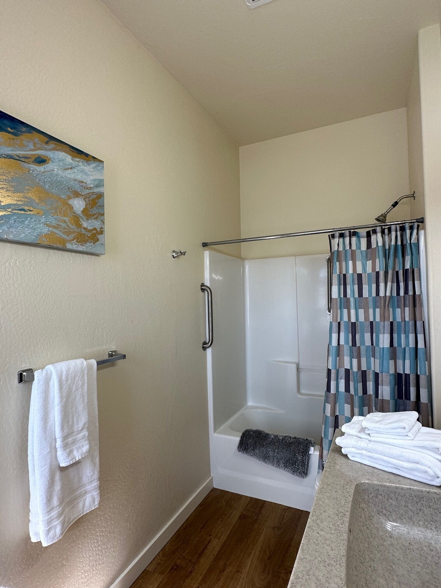 A bathroom with a shower, a towel rack, a painting, and a sink.