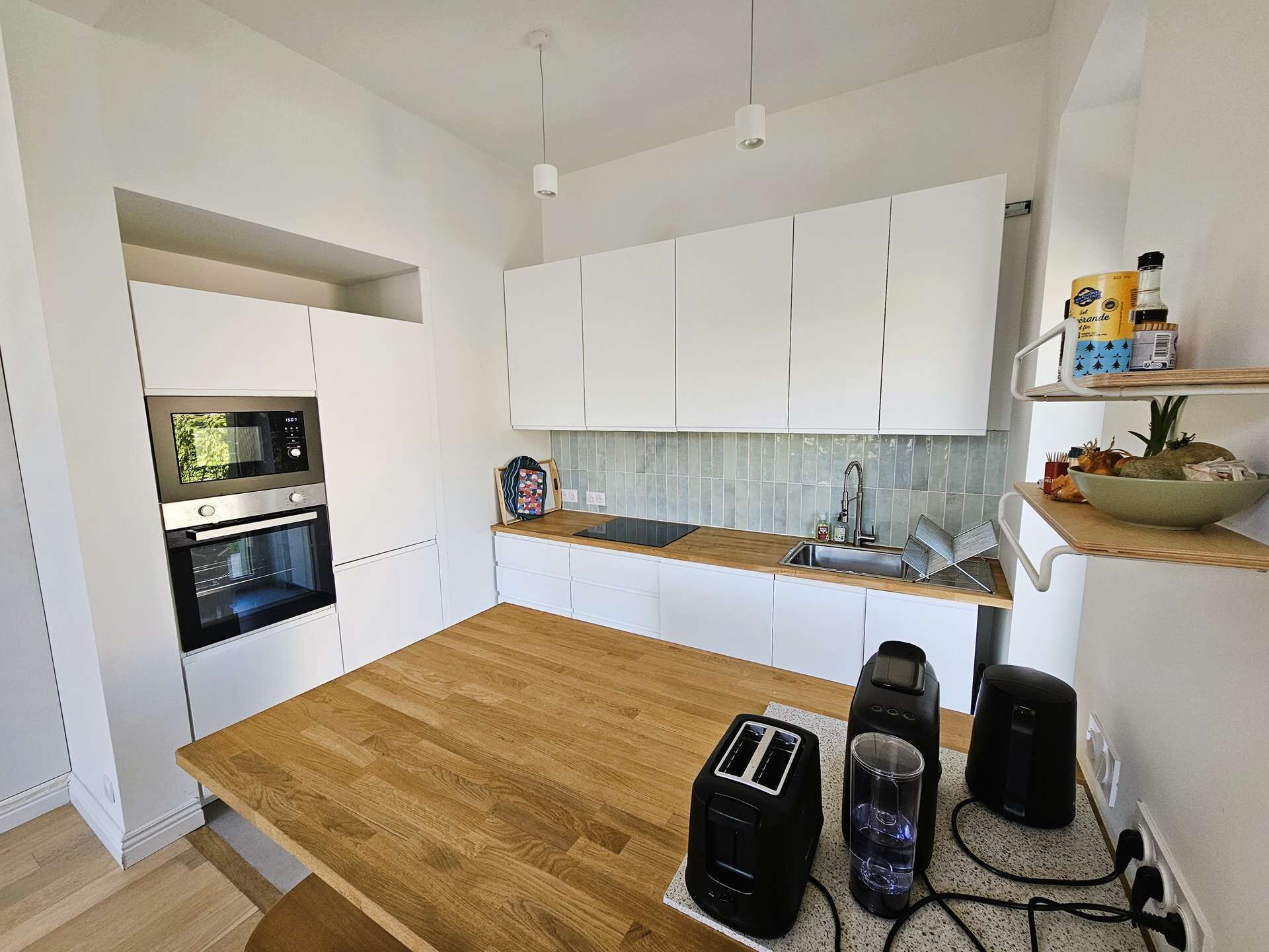 A modern kitchen with white cabinets, a wooden countertop, a built-in oven, a microwave, a sink, and a toaster.
