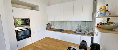 A modern kitchen with white cabinets, a wooden countertop, a built-in oven, a microwave, a sink, and a toaster.