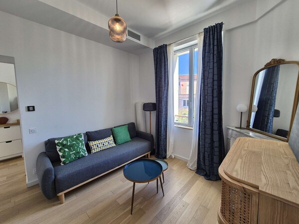 A modern room with a sofa, a small table, a mirror, and a window with curtains.