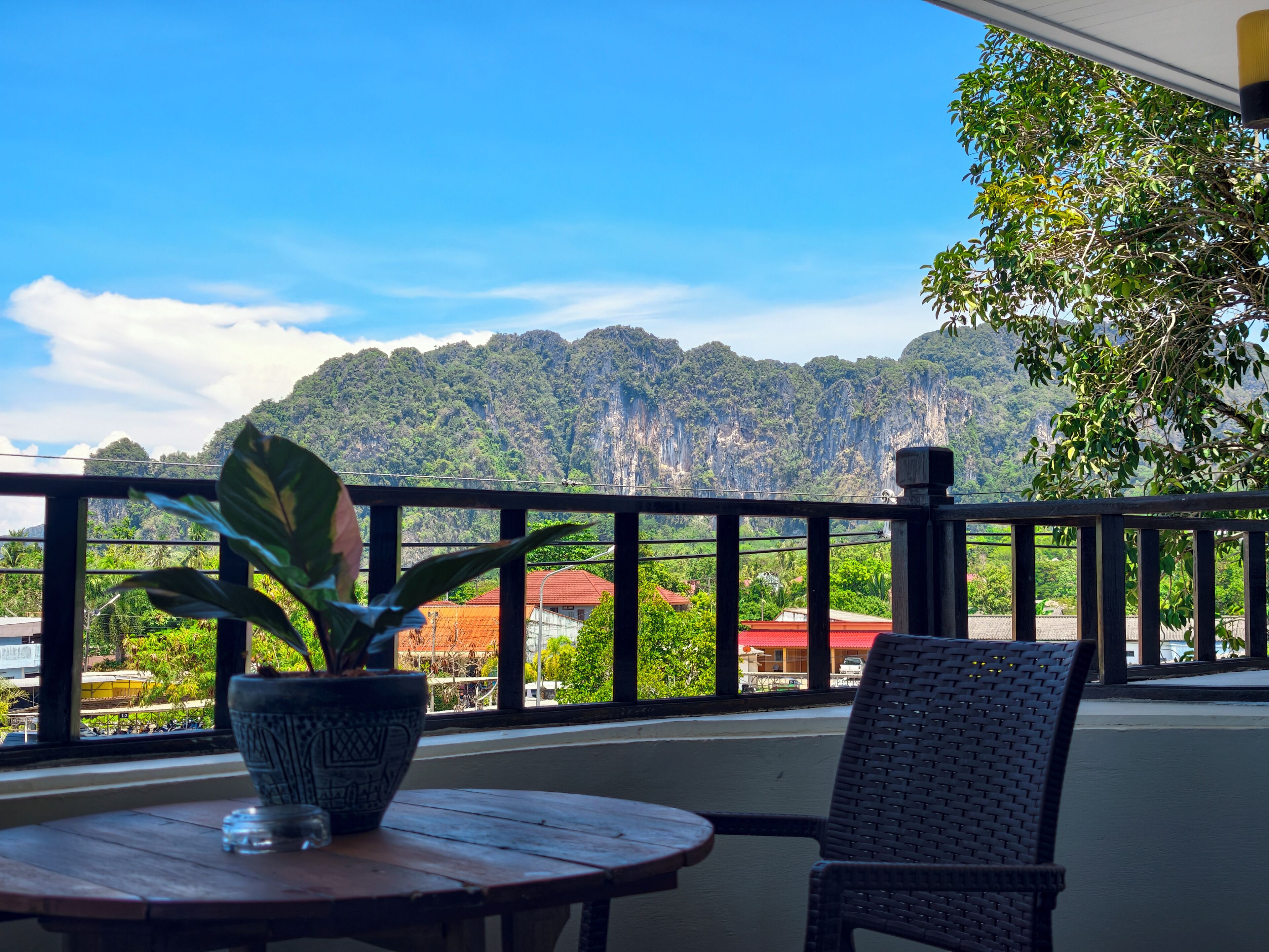Un balcon donnant sur un paysage montagneux, une plante en pot et une chaise en osier.