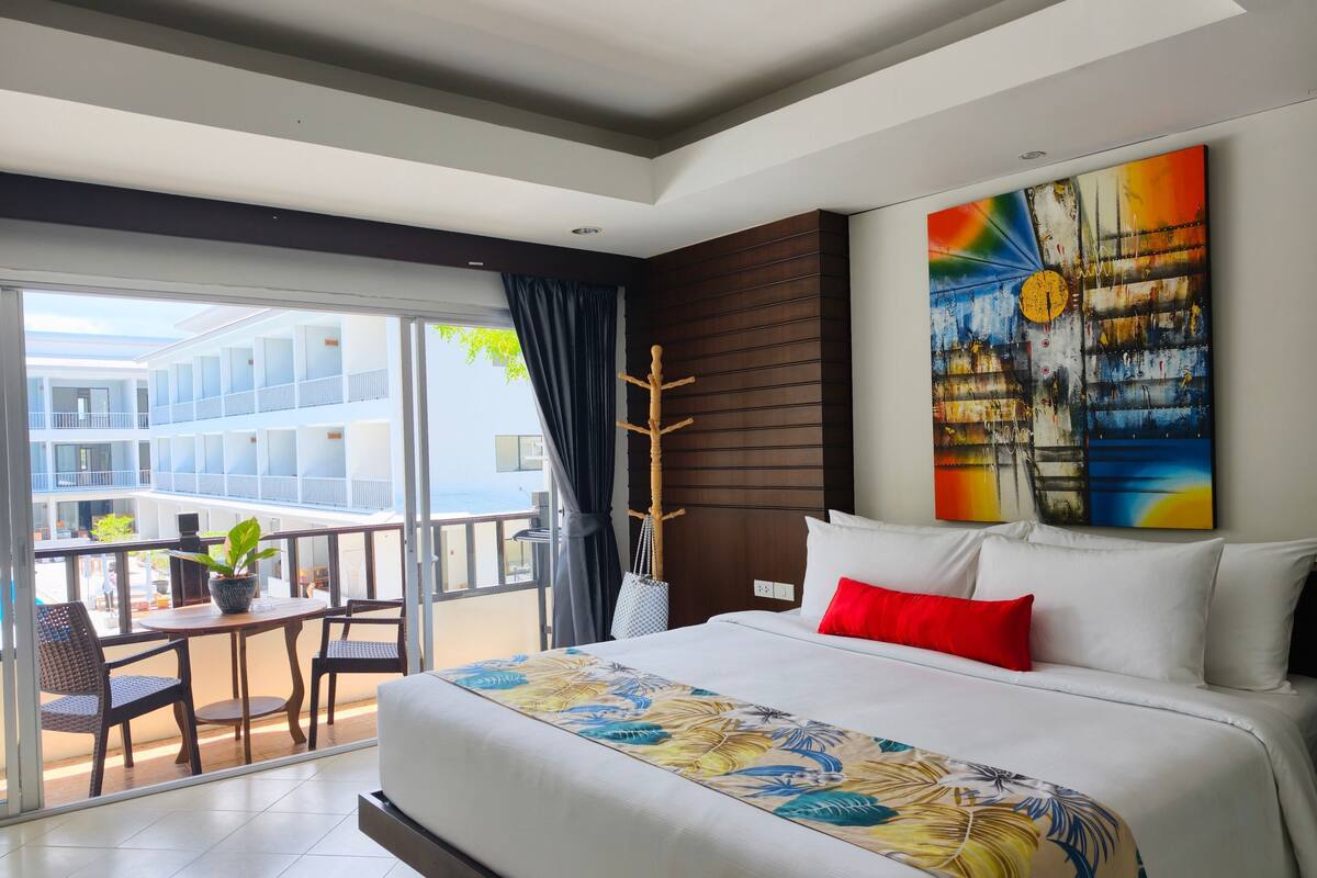 Een hotelkamer met balkon, een bed met bloemenbeddengoed, een schilderij aan de muur en uitzicht op het gebouw.