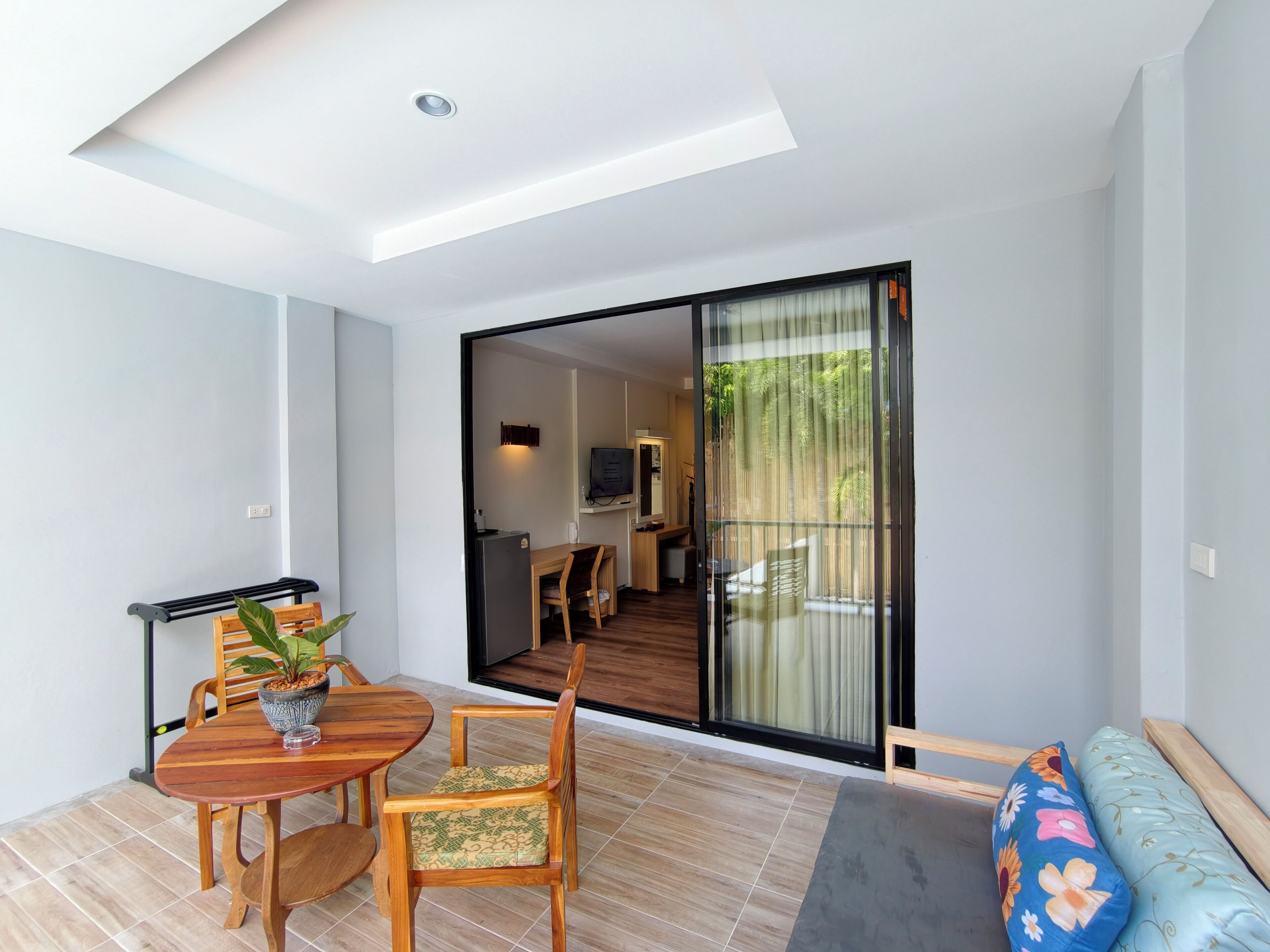 A modern living room with a wooden dining table, chairs, a sofa, and a large sliding glass door leading to a balcony.