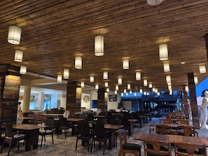 Restaurante com teto e mesas de madeira, uma estátua e vista para o exterior.