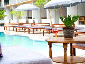 Uma área à beira da piscina com espreguiçadeiras, guarda-sóis e uma mesa com um vaso de planta e um copo de vinho tinto.