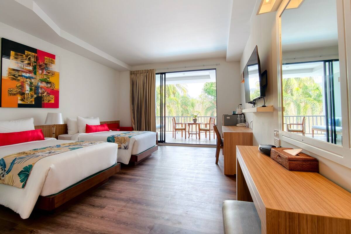 Een hotelkamer met twee bedden, een bureau, een televisie en een balkon met stoelen.