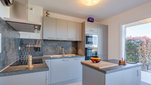 A modern kitchen with a central island, built-in oven, and a large window offering a view of greenery.