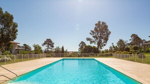A rectangular swimming pool with clear blue water, surrounded by a tiled deck and a metal fence.