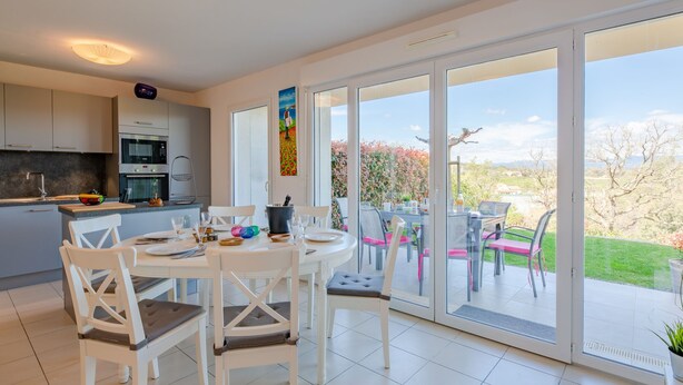 A modern kitchen with white cabinets, a dining area with white chairs, and a large sliding glass door leading to a patio with outdoor seating.
