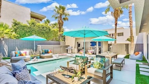 A modern outdoor pool area with lounge seating, umbrellas, and a well-maintained lawn.