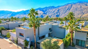A modern residential area with compact housing, palm trees, and mountains in the background.
