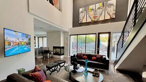 A spacious living area with a large flat-screen TV, a sofa with colorful cushions, a coffee table, and a staircase.