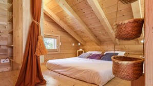 A cozy wooden cabin bedroom with a bed, pillows, and a hanging basket.