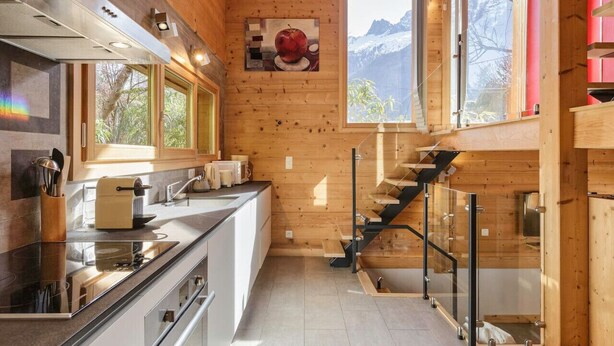 A modern kitchen with wooden walls, a stainless steel stove, and a glass staircase.