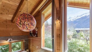 A wooden interior with a large window, a hanging light fixture, and a kitchen area with appliances.