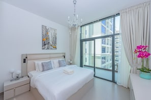 Un dormitorio moderno con una cama grande, una araña, un cuadro de un paisaje urbano y vistas de edificios a través de un ventanal.