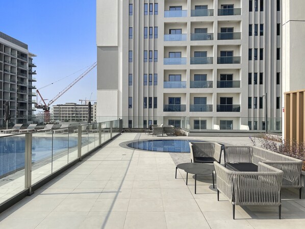 Un área de piscina en la azotea con sillones de descanso y vistas a un rascacielos.